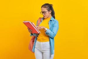 verwarde vrouw student in denim kleding met rugzak, lezen in het werk notebook geïsoleerd op gele achtergrond. onderwijs op de middelbare school universiteit college concept foto