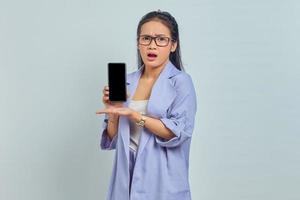 portret van verraste jonge aziatische vrouw die een leeg schermtelefoon met palm toont die op witte achtergrond wordt geïsoleerd foto
