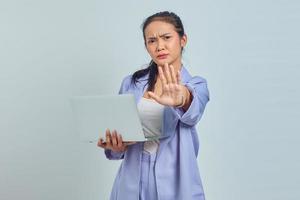 portret van serieuze jonge aziatische vrouw die laptop vasthoudt en met uitgestrekte hand staat met stopgebaar geïsoleerd op een witte achtergrond foto