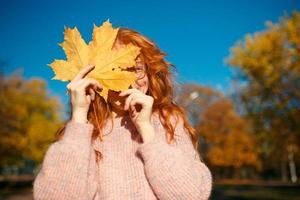 portretten van een charmant roodharig meisje met een schattig gezicht. meisje poseren in herfst park in een trui en een koraalkleurige rok. in de handen van een meisje een geel blad foto