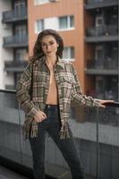 prachtige glamour brunette vrouw met geruite jas poseren op modern balkon met prachtig uitzicht op de stad. portret van een stijlvolle modieuze vrouw met lange benen, zwarte jeans dragen in balkon foto