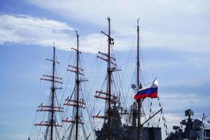 de russische vlag tegen de achtergrond van de masten van een zeilboot en oorlogsschepen. foto