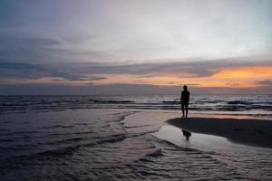 silhouet van een vrouw die op het strand staat bij zonsondergang foto