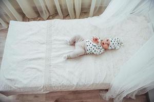 pasgeboren baby gekleed in een wit pak en zwarte sterren is een wit zacht bed in de studio foto