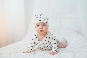 pasgeboren baby gekleed in een wit pak en zwarte sterren is een wit zacht bed in de studio foto