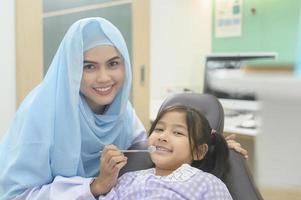 een klein schattig meisje met tanden onderzocht door moslim tandarts in tandheelkundige kliniek, tanden check-up en gezond gebit concept foto