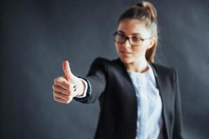 jonge vrouw toont duim omhoog staan op zwarte achtergrond, focus op hand. foto