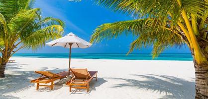 prachtig tropisch eilandlandschap, twee ligbedden, ligstoelen, parasol onder palmboom. wit zand, uitzicht op zee met horizon, idyllische blauwe lucht, rust en ontspanning. inspirerend strandresorthotel foto