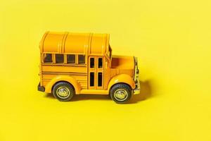 ontwerp eenvoudig gele klassieke speelgoedauto schoolbus geïsoleerd op gele kleurrijke achtergrond. veiligheid dagelijks vervoer voor kinderen. terug naar schoolconcept. onderwijs symbool, kopieer ruimte foto