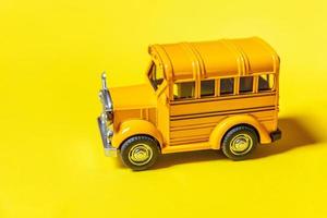 ontwerp eenvoudig gele klassieke speelgoedauto schoolbus geïsoleerd op gele kleurrijke achtergrond. veiligheid dagelijks vervoer voor kinderen. terug naar schoolconcept. onderwijs symbool, kopieer ruimte foto