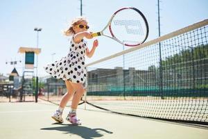 schattig klein meisje tennist buiten op de tennisbaan foto