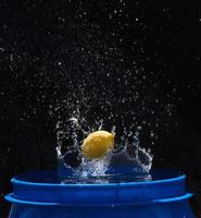 gele citroen die in het blauwe water valt op een zwarte achtergrond foto