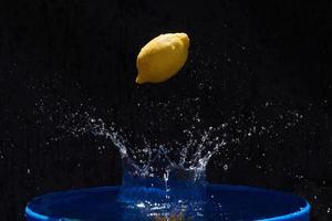 sappige gele citroen valt in water op een zwarte achtergrond foto