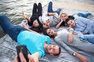 portret van gelukkige jonge vrienden op de pier aan het meer. terwijl u geniet van de dag en selfie doet. foto
