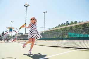 schattig klein meisje tennist buiten op de tennisbaan foto