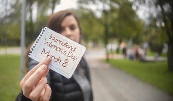 mooie Spaanse vrouw in het midden van een park met in haar hand een papier met de boodschap internationale vrouwendag foto