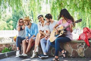 groep gelukkige vrienden met gitaar. terwijl een van hen gitaar speelt en anderen hem een applaus geven foto