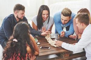 groep creatieve vrienden zitten aan houten tafel. mensen die plezier hebben tijdens het spelen van een bordspel foto