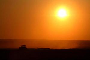 ondergaande zon achter de landbouw die zijn velden bewerkt foto