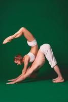 mooie sportieve vrouw en man in witte kleren doen yoga asana's samen binnen op groene achtergrond foto