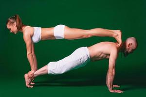 mooie sportieve vrouw en man in witte kleren doen yoga asana's samen binnen op groene achtergrond foto