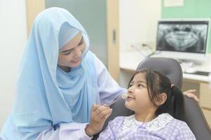 een klein schattig meisje met tanden onderzocht door moslim tandarts in tandheelkundige kliniek, tanden check-up en gezond gebit concept