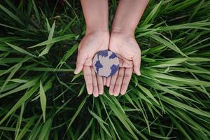 red de aarde voor een duurzaam levensstijlconcept, bescherm de planeet aarde voor duurzame hulpbronnen. menselijke handen met wereldbol symbool op gras bladeren achtergrond. Earth Day en duurzaamheidsontwikkeling. foto