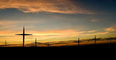 silhouet van christelijk kruis en windturbines bij zonsondergang foto
