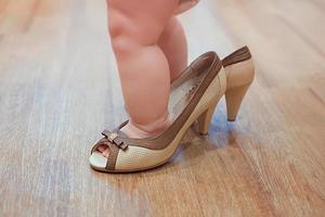 kleine baby-baby die volwassene speelt in schoenen met hak van de moeder foto