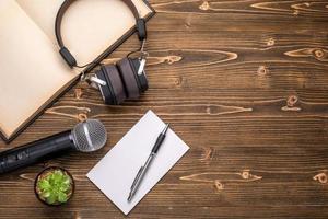 microfoon, koptelefoon, boek en papieren notitie op bruin houten bord. leren over spreken concept foto