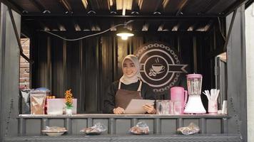 mooie glimlachende aziatische serveerster die de container van de cafécabine bewaakt foto