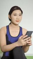 Aziatische vrouw zit ontspannen mobiel te spelen na het beëindigen van yoga thuis foto