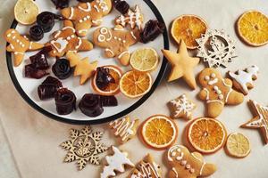 peperkoek kerstkoekjes en gedroogde sinaasappel en kruiden op witte tafel. pastel, jam in rolletjes op een bord foto