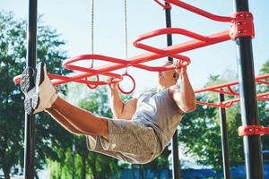 gespierde man met mooie torso oefenen op horizontale balken op de achtergrond van een wazig park. jonge man doet pull-ups buitenshuis foto