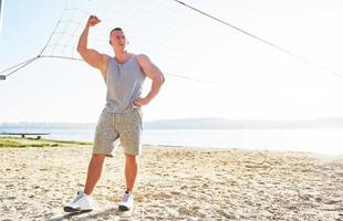 een atletische man kijkt naar de kust op het wilde zandstrand. mannelijke en sportieve man met naakte torso doet avondtraining tegen de zeeprijs. zomer work-out training buiten foto