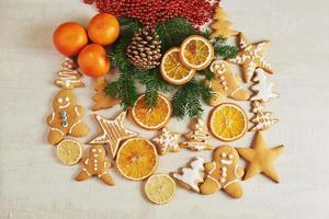 peperkoek kerstkoekjes en gedroogde sinaasappel en kruiden op witte tafel. stoelen kerstbomen, kegels en kerstversieringen foto