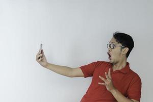 wow gezicht van jonge aziatische man geschokt wat hij ziet in de smartphone op geïsoleerde grijze achtergrond. foto