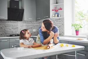 gelukkige familie in de keuken. vakantie voedsel concept. moeder en dochter bereiden het deeg voor, bakken koekjes. gelukkige familie bij het maken van koekjes thuis. zelfgemaakt eten en kleine helper foto