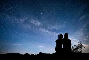 melkweg met silhouet van mensen. landschap met nachtelijke sterrenhemel. staande man en vrouw op de berg met sterrenlicht. knuffelend paar tegen paarse melkweg. foto