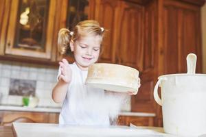 een gelukkig meisje draagt een deeg. baby maakt diner in kokskostuum foto