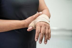 aziatische dame van middelbare leeftijd gebruikt elastisch verband om het quervain-syndroom bij de hand en vinger op kantoor te behandelen. foto