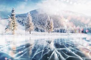 blauw ijs en scheuren op het oppervlak van het ijs. bevroren meer in de winterbergen. het sneeuwt. de heuvels van dennen. winter. karpaten oekraïne europa foto