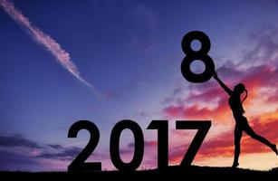 silhouet van het meisje dat de nummers van het nieuwe jaar in de zonsondergang vasthoudt. concept van vervanging 2017 tot 2018 foto