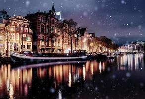 mooie nacht in amsterdam. nachtverlichting van gebouwen en boten in de buurt van het water in het kanaal tijdens een sneeuwstorm. bokeh lichteffect, zacht filter foto