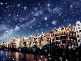 mooie nacht in amsterdam, verlichting van gebouwen en boten in de buurt van het water in het kanaal tijdens een sneeuwstorm. bokeh lichteffect, zacht filter foto