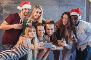 groep mooie jonge mensen die selfie doen in het nieuwe jaarfeest, beste vrienden, meisjes en jongens die samen plezier hebben, mensen met een emotionele levensstijl poseren. hoeden kerstmannen en champagneglazen in hun handen foto