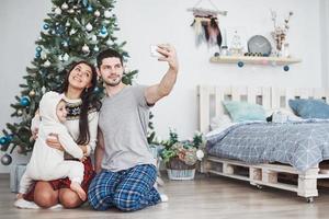 familie verzameld rond een kerstboom, met behulp van een tablet foto