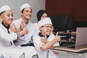 gelukkige moslimfamilie die videogesprek doet en plezier heeft voor een laptop met duim omhoog gebaar tijdens eid mubarak-viering foto