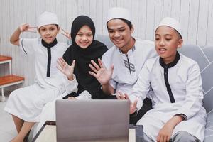 gelukkige moslimfamilie doet videogesprek vooraan een laptop met hallo of groet gebaar met de hand op eid mubarak-viering foto
