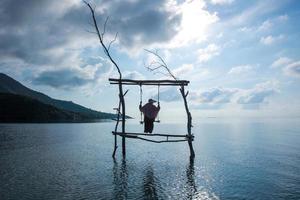 zwart silhouet van vrouw in zomerhoed die op houten schommeling over ondiep en kalm zeewater slingert bij Karimun Jawa foto